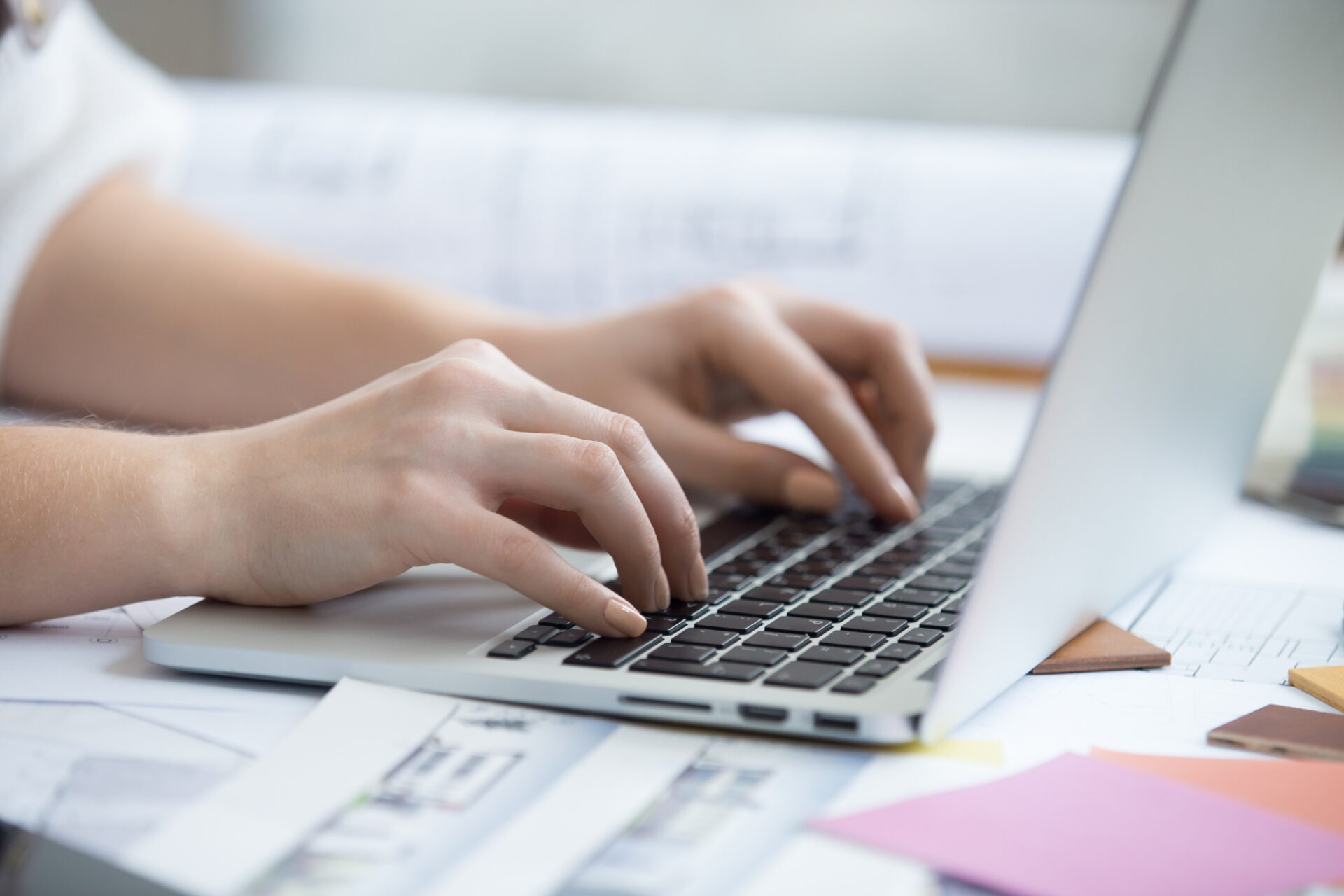 Mains tapant sur un ordinateur portable entouré de documents