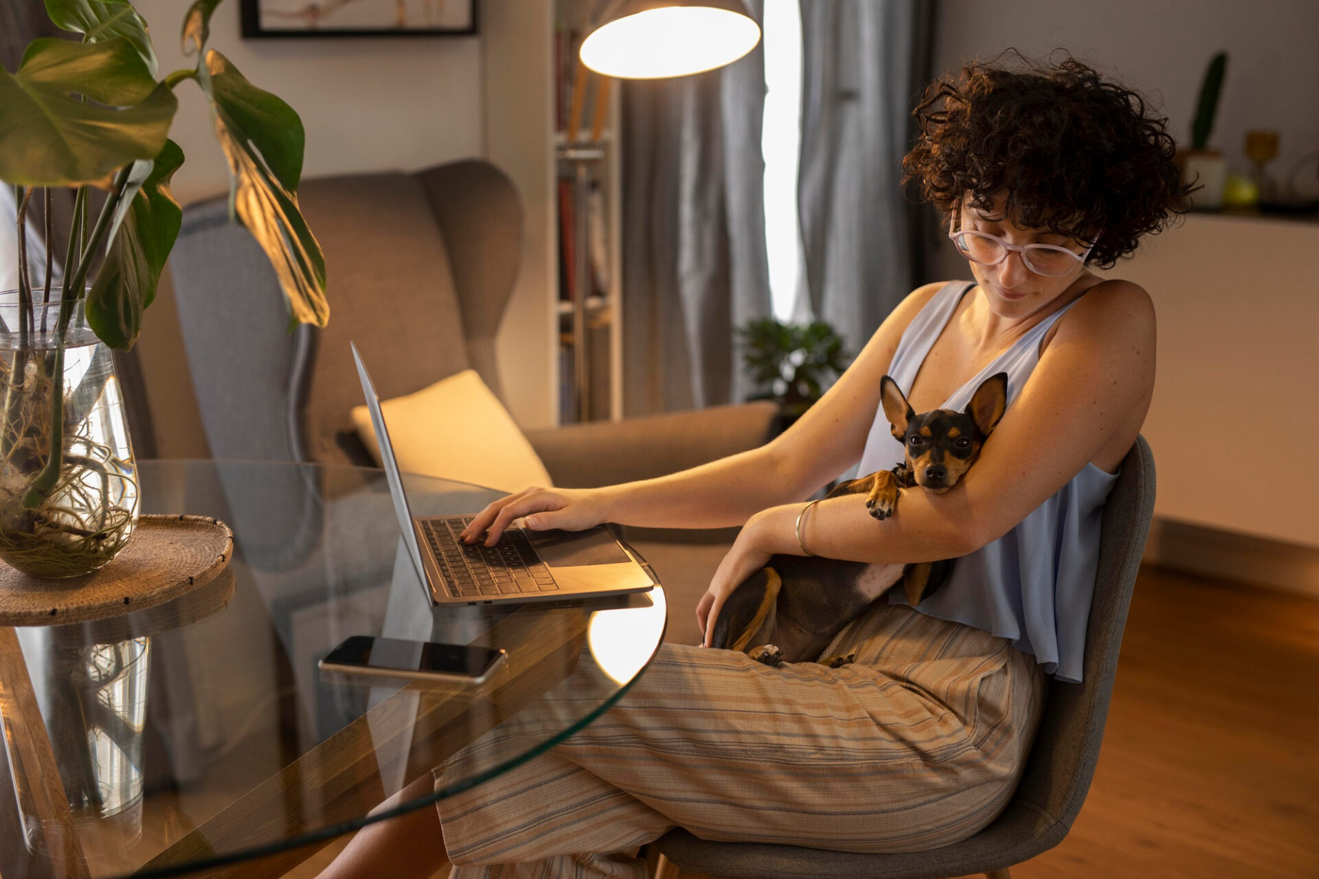 Femme assise chez elle devant un ordinateur portable avec un chien sur ses genoux
